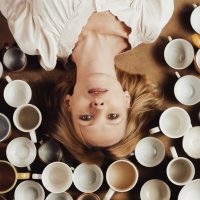 A middle aged woman looks into the camera and there are many empty cups on the floor. The concept of deadline, nervous exhaustion, staying awake.
